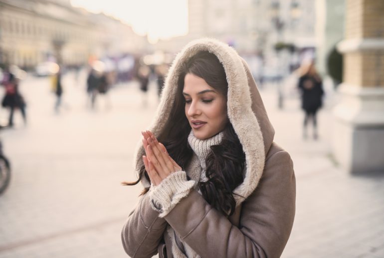 Young woman warming hands while standing on the street in cold weather.