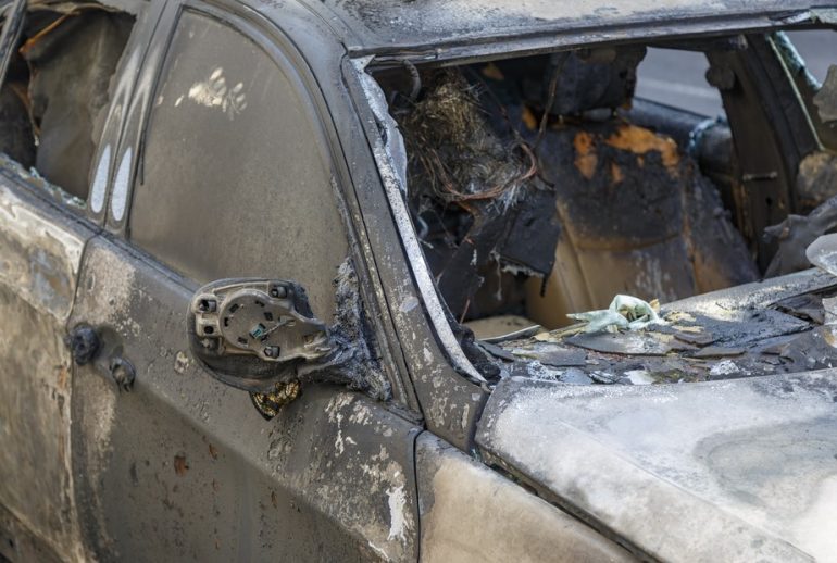 Windows shatter from the explosion. Setting fire to cars of a terrorist attack. Remains of a burned car. Burned out car on roadside down in the middle of the street. Burnt new car, vandalism, mafia.