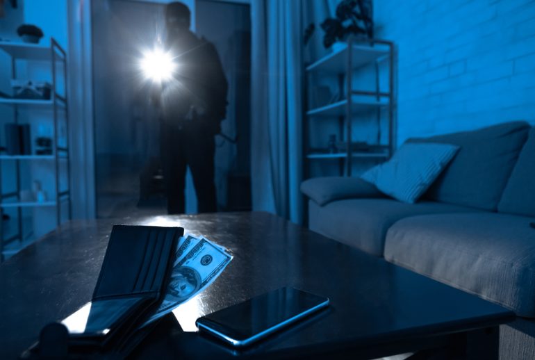 Burglary Concept. Robber breaking into modern apartment, using flashlight, cash and cell phone lying on the table