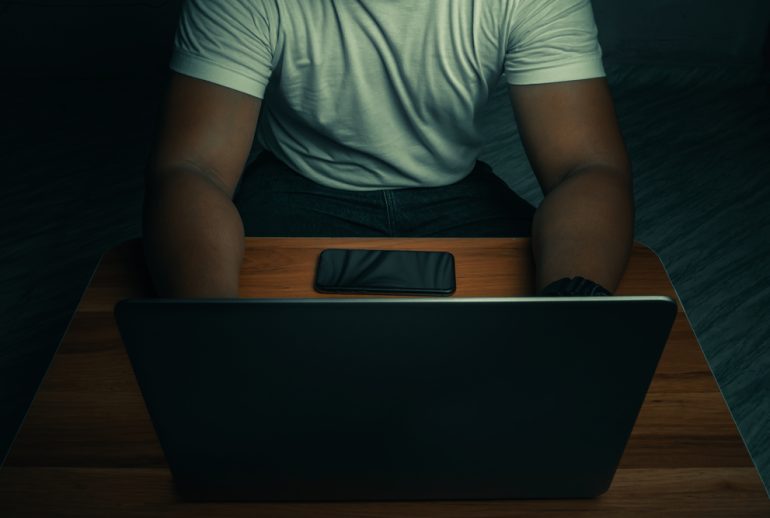 A man in a white shirt sits on a laptop in a dark room. with light shining down. internet concept addiction.topview.